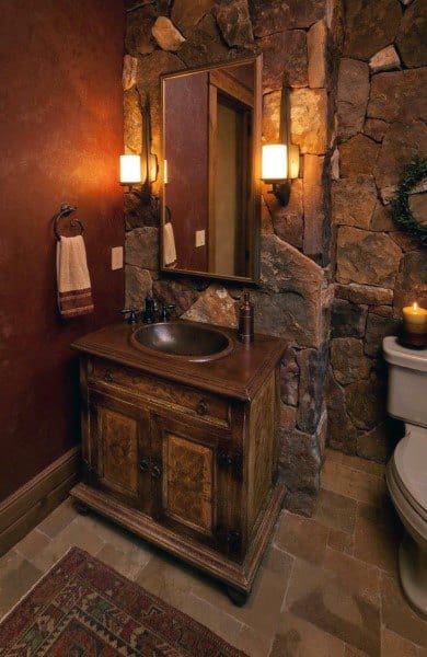 Rustic half bath with stone walls, wooden vanity, mirror, and warm lighting