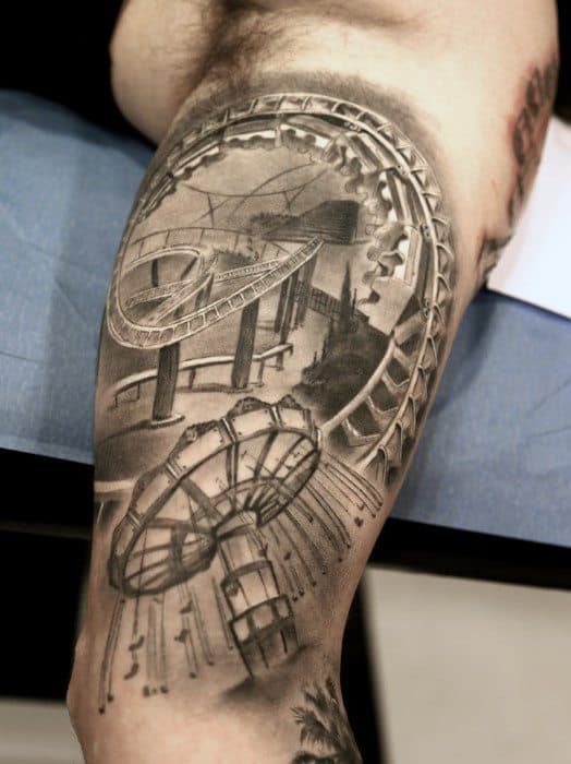 Realistic amusement park tattoo with a roller coaster, spinning swing ride, and detailed shading on the upper arm.