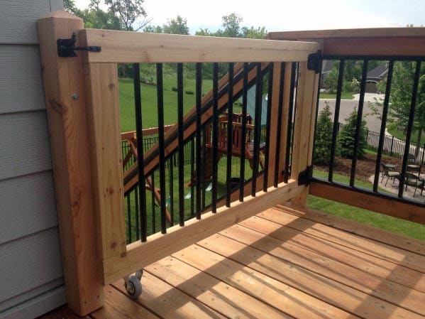 Wooden deck gate with black metal bars and a rolling wheel underneath