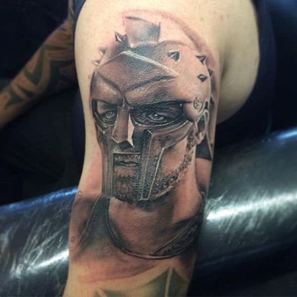 Tattoo of a fierce gladiator clad in a spiked helmet on person's upper arm
