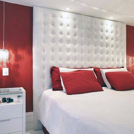 Bedroom with white tufted headboard, bold red accent wall, and pillows, white bedding, and a small bedside table