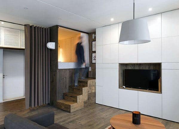 Modern studio with wooden stairs, built-in TV unit, and cozy loft bed.