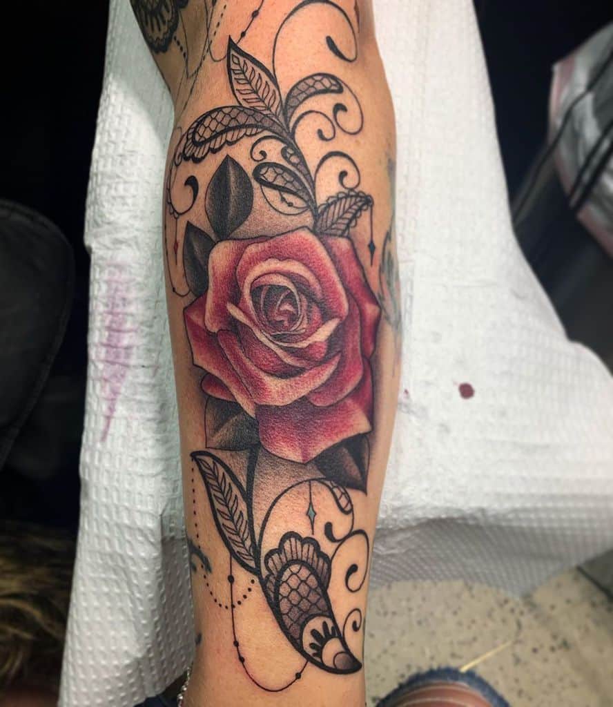 Leg tattoo featuring a realistic red rose with intricate lace, filigree swirls, and delicate beaded chain details.