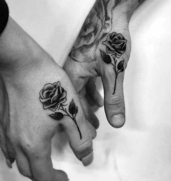 Matching rose tattoos on the thumbs, symbolizing love, beauty, and a shared romantic connection between the couple.