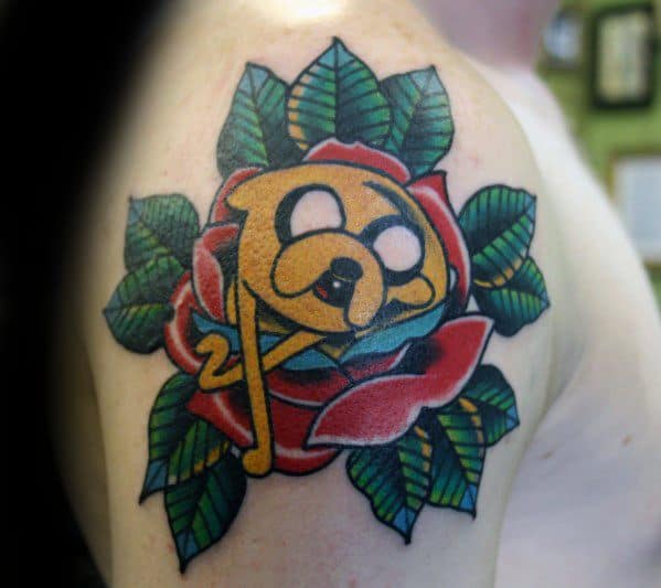 Adventure Time tattoo of Jake the Dog nestled inside a traditional red rose with green leaves, inked on the upper arm.