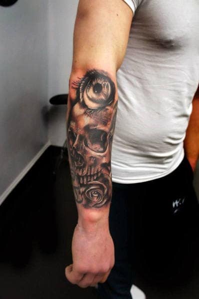 Black and grey forearm tattoo featuring a realistic skull, detailed eye, and roses, creating a dark and dramatic design.