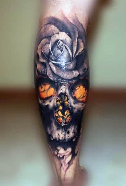 Dark tattoo of a skull with glowing orange eyes and a realistic rose on top, creating a haunting and dramatic design on the leg.