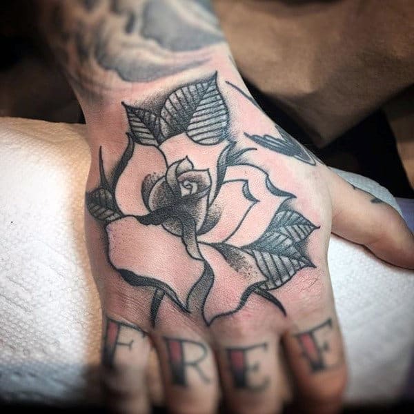 A hand tattoo of a rose with detailed leaves, and "FREE" inked across the fingers