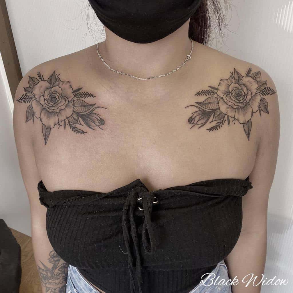 Floral shoulder tattoos featuring detailed black and grey roses with leaves, located on both shoulders