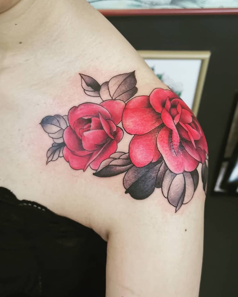 Bright red rose shoulder tattoo with detailed shading, paired with black and grey leaves, placed on the upper arm