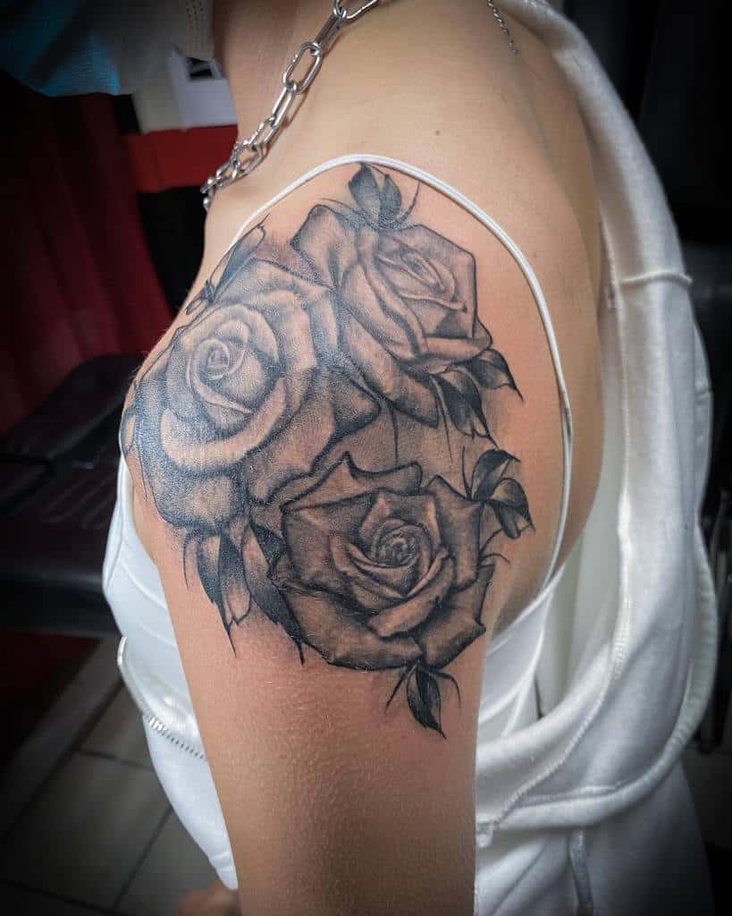 A tattoo of three shaded black roses elegantly graces the shoulder