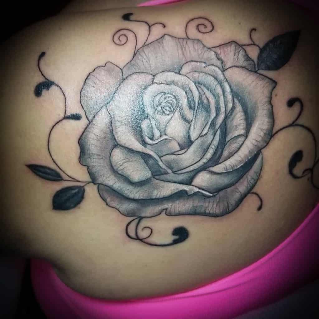 A stunning black and gray rose tattoo with intricate leaves and swirls on the shoulder