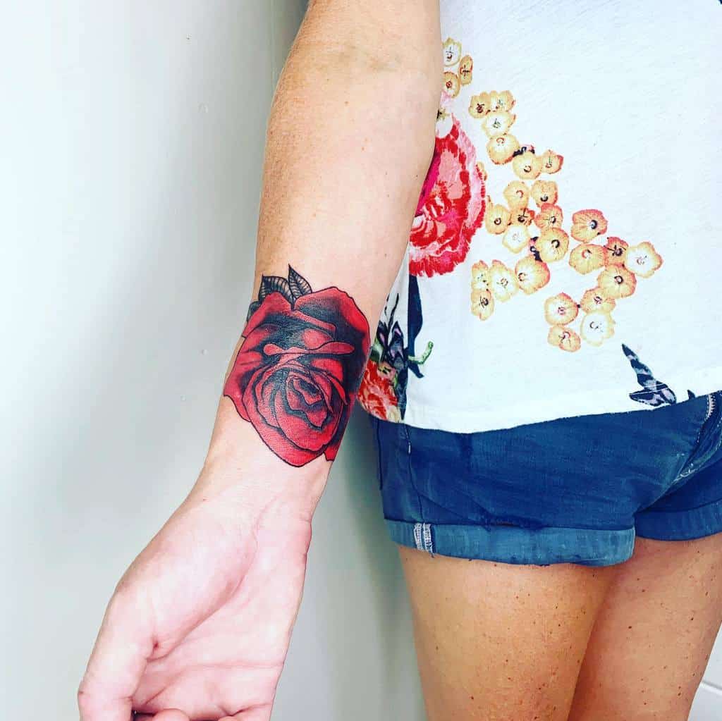 Bold red rose tattoo with black shading, placed on the inner wrist, featuring detailed petals and leaves