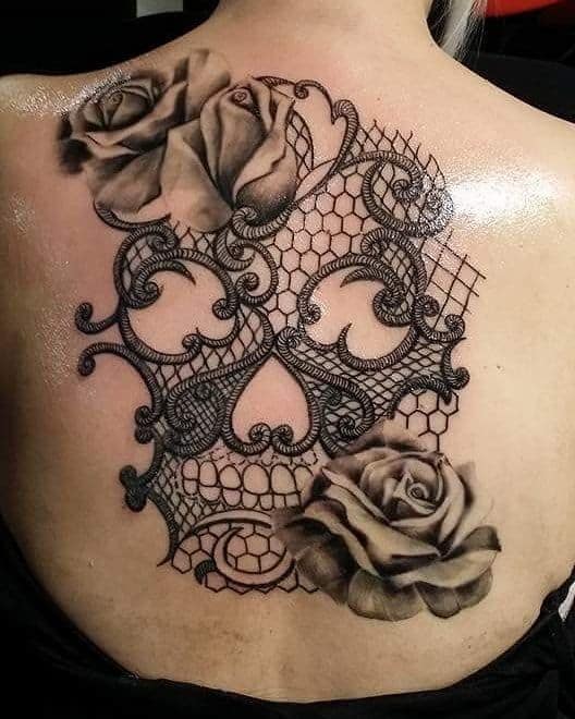 Elegant back tattoo featuring realistic shaded roses with intricate black lace patterns and ornamental swirls for a bold yet delicate look.