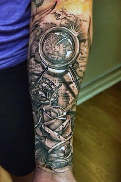 A stunning sleeve design featuring a forearm tattoo of a compass, map, and roses, all intricately detailed in black and gray ink