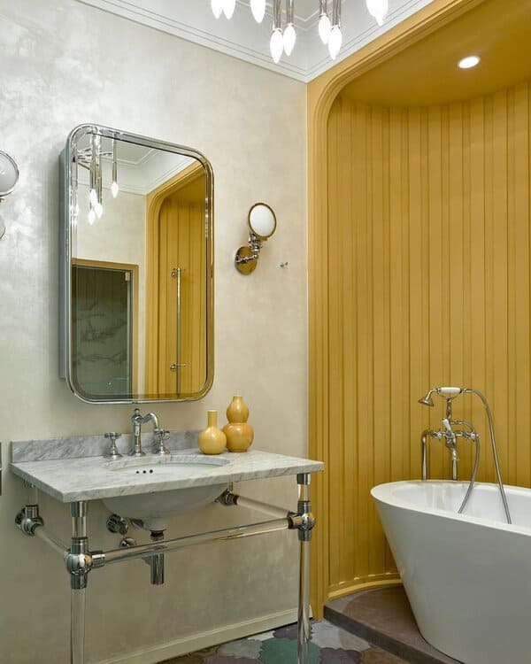 Freestanding tub under an arched mustard alcove with a chrome console sink, marble top, and plaster walls.