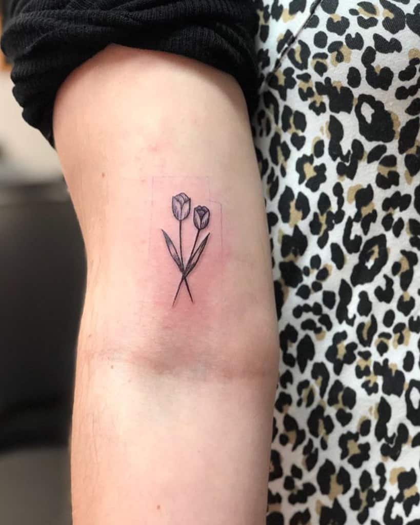 A small, minimalist tulip tattoo on the inner elbow, featuring two delicate flowers with fine black-line detailing and subtle shading.