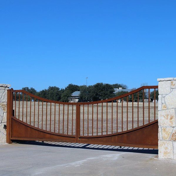 Rustic driveway gate with arched rusted steel frame and vertical bars.