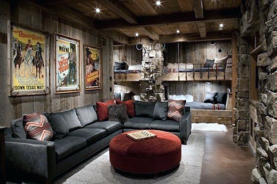 Rustic living room with a gray sectional, red ottoman, bunk beds, stone walls, and vintage movie posters create a cozy home theater