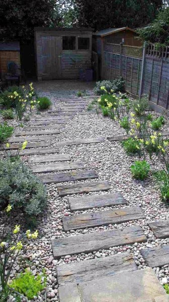 Garden with stone walkway, surrounded by yellow flowers and greenery, leading to a wooden shed