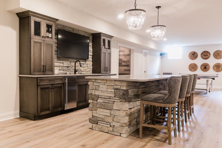 Rustic basement kitchen with stone island, wooden cabinets, and crystal chandeliers.
