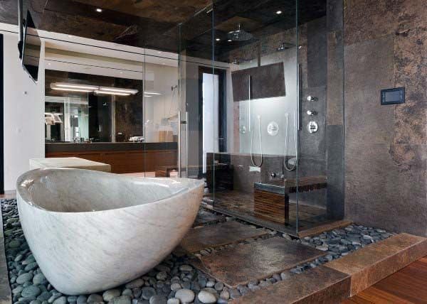 Rustic bathroom with a stone bathtub, pebble floor, and glass-enclosed shower