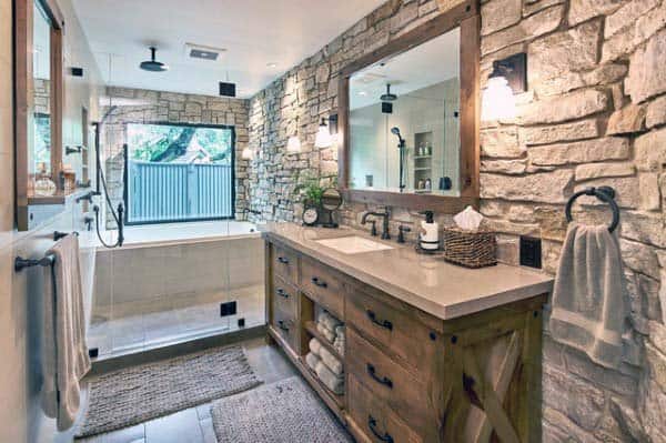 Rustic bathroom with stone walls, wooden vanity, large mirror, and walk-in shower