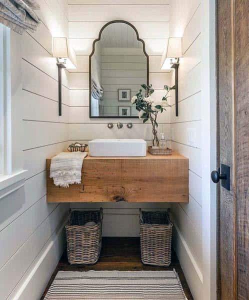 Rustic bathroom with wooden vanity, mirror, wall lamps, and woven baskets
