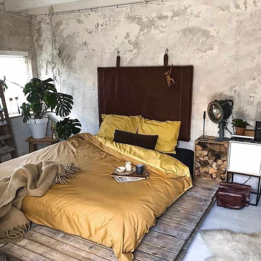 Rustic bedroom with exposed concrete wall, yellow bedding, and platform wooden bed.