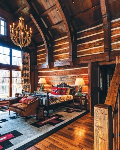 Rustic cabin bedroom with log walls, chandelier, and large patterned rug.