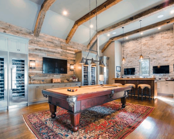 Rustic billiard room with exposed beams, reclaimed wood walls, and a pool table on a Persian rug.