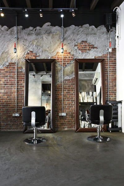 Industrial barbershop with exposed brick walls, large mirrors, and black leather chairs.