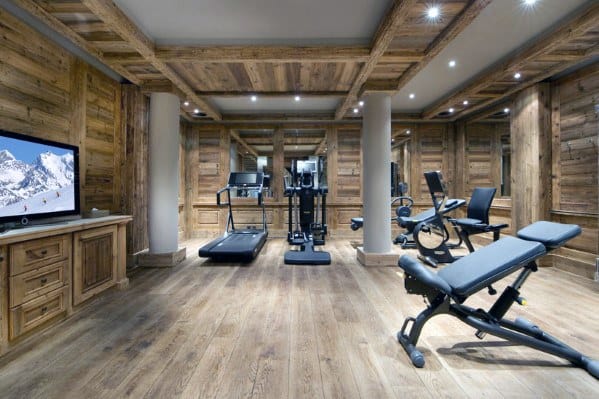 Rustic home gym with wooden walls, hardwood flooring, cardio machines, and a flat-screen TV.