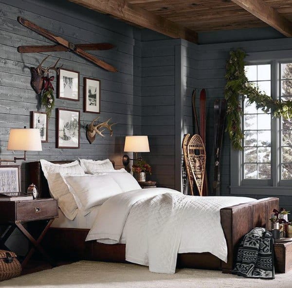 Rustic bedroom with antler wall art, vintage skis, framed photos, and cozy white bedding.