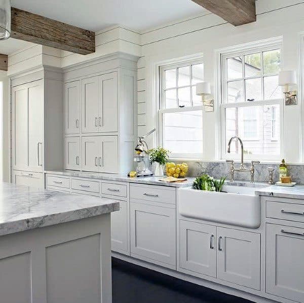 Rustic kitchen with white cabinets, farmhouse sink, marble countertops, and wooden beam accents.