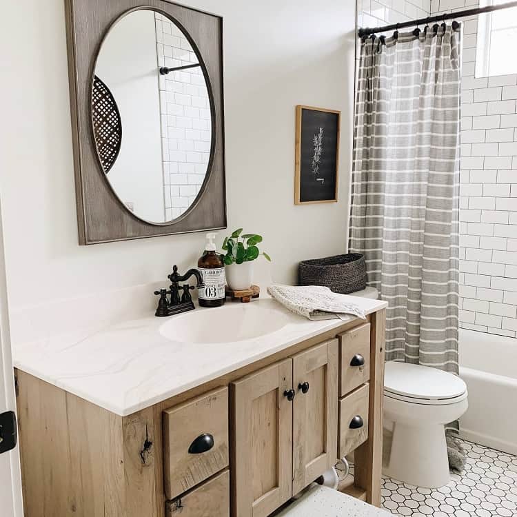 Cozy farmhouse bathroom with a wooden vanity, round mirror, potted plant, and striped shower curtain
