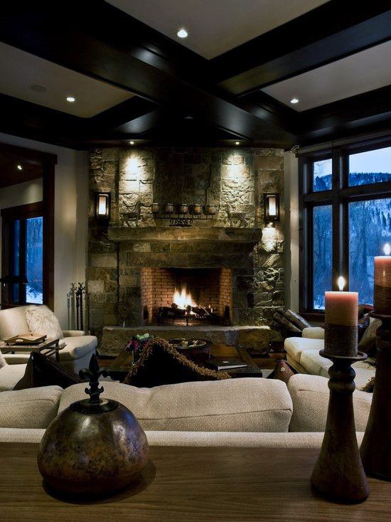 Rustic living room with stone fireplace, exposed beams, beige sofas, and warm ambient lighting.