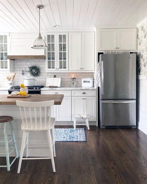 Rustic white kitchen with wood countertops, stainless steel fridge, and shiplap walls.