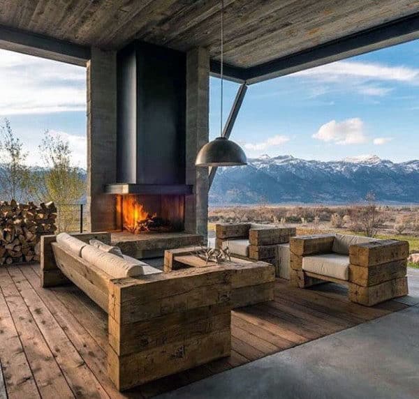 Rustic patio with wooden furniture, a fireplace, and a view of snowy mountains under a modern, industrial roof