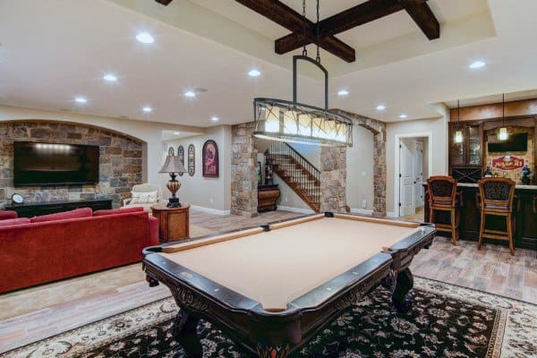 Rustic basement with wood beam ceiling, recessed lighting, pool table, bar area, and stone accents.