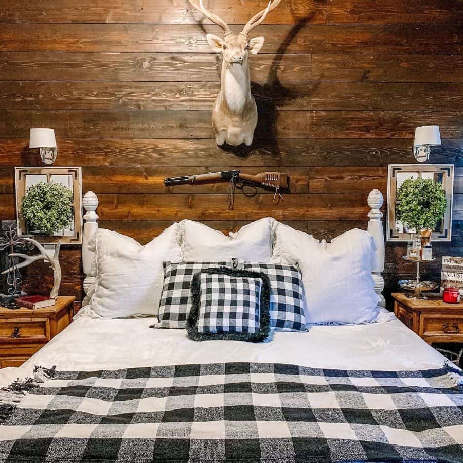 Rustic bedroom with a mounted deer head, white bedding, and black-and-white plaid accents against a wooden wall
