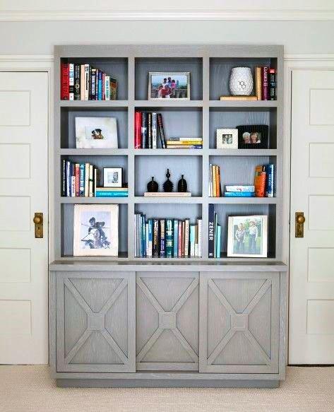 Grey bookshelf with books, framed photos, and decor items against a wall with white doors on each side