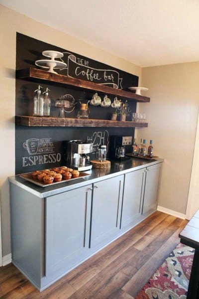 Coffee bar with grey cabinets, chalkboard wall, wooden shelves, and pastries on display.