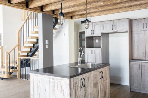 Rustic kitchen with light wood cabinets, exposed beam ceiling, pendant lights, and modern sink island.