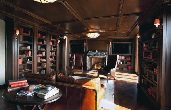 Cozy library with leather couches, armchairs, wooden bookshelves, and a lit fireplace