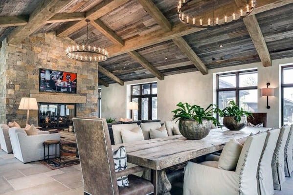 A rustic wood ceiling with exposed beams complements the stone fireplace and farmhouse dining table.