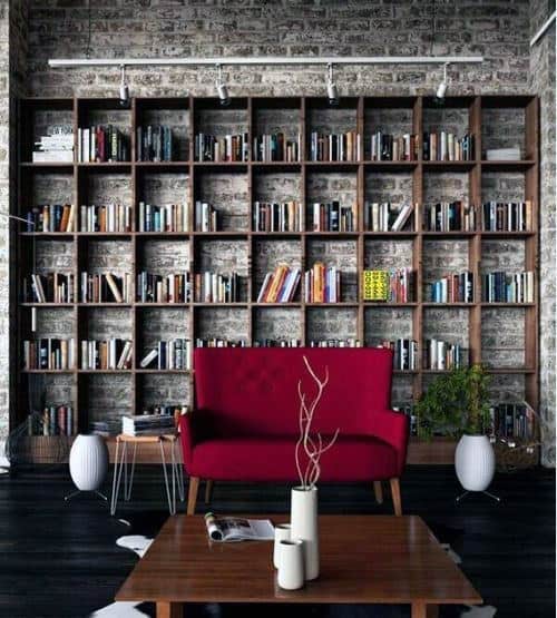 A cozy reading nook with a red sofa, wooden bookshelves filled with books, and white vases on wooden tables