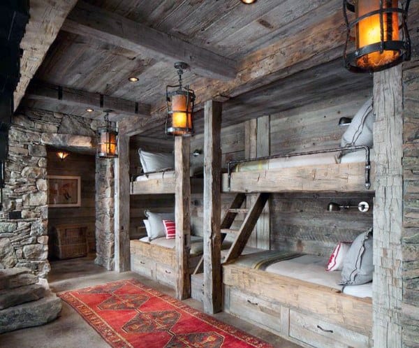 Rustic log cabin with bunk beds, stone walls, warm lighting, and a red patterned rug