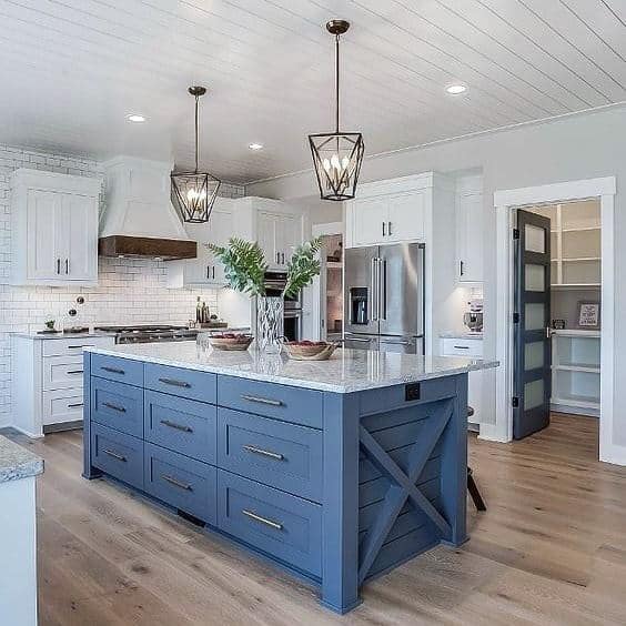 Rustic kitchen with blue island, white cabinets, pendant lights, and a farmhouse sink.