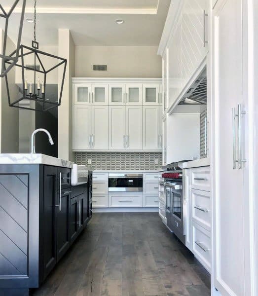 Modern rustic kitchen with white cabinets, black island, pendant lights, and hardwood flooring.